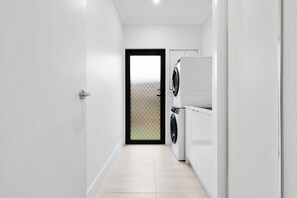 A laundry room with a washing machine and dryer, a tiled floor, and a door leading to another room. - The Pinnacle | Luxury 4BR Home | Alfresco Living (Burpengary East)