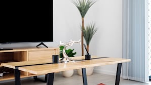 Ein modernes Wohnzimmer mit einem Holztisch, einer dekorativen Metallskulptur, einem Fernseher und einer Topfpflanze.