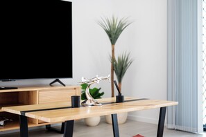 A modern living room with a wooden coffee table, a decorative metal sculpture, a television, and a potted plant. - The Pinnacle | Luxury 4BR Home | Alfresco Living (Burpengary East)