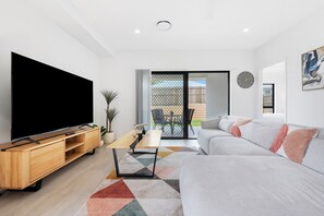 Una sala moderna con televisor de pantalla plana, mueble de entretenimiento de madera, sofá, mesa de centro y una alfombra colorida.