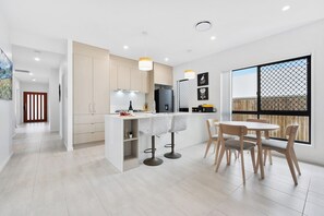 A modern kitchen with a dining area, featuring a large window, a kitchen island, and a dining table with chairs. - The Pinnacle | Luxury 4BR Home | Alfresco Living (Burpengary East)