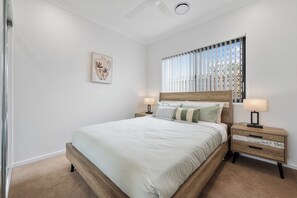 Ein Schlafzimmer mit einem Bett, Nachttischen, einem Fenster mit Jalousien und einem Deckenventilator.