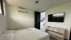 Un dormitorio con cama, televisor, aparador de madera y una escalera al fondo.