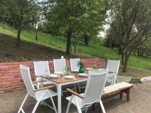 An outdoor dining area with a brick wall, white chairs, and a table set for four. - Two holiday homes on one estate in the heart of Podravina (Đurđevac)