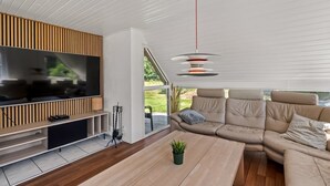 Uma sala de estar moderna com televisão de tela plana, painel de parede em madeira, sofá bege e uma luminária pendente.