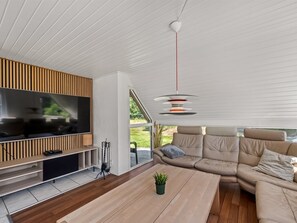 Ein modernes Wohnzimmer mit Flachbildfernseher, Holzpaneelwand, beiger Couch und einer hängenden Pendelleuchte.