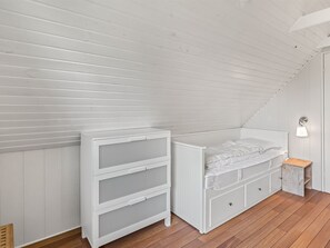 Ein Schlafzimmer mit schrägem Dach, einem Bett mit Stauraum, einem kleinen Holzschemel und einer Wandleuchte.