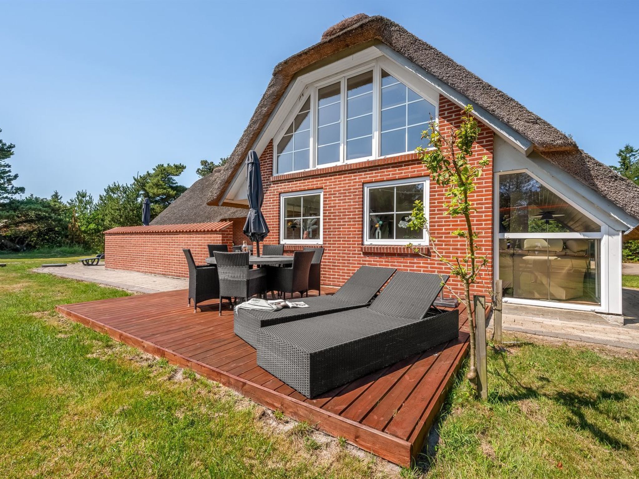 A house with a thatched roof, a deck with outdoor furniture, and a large window.