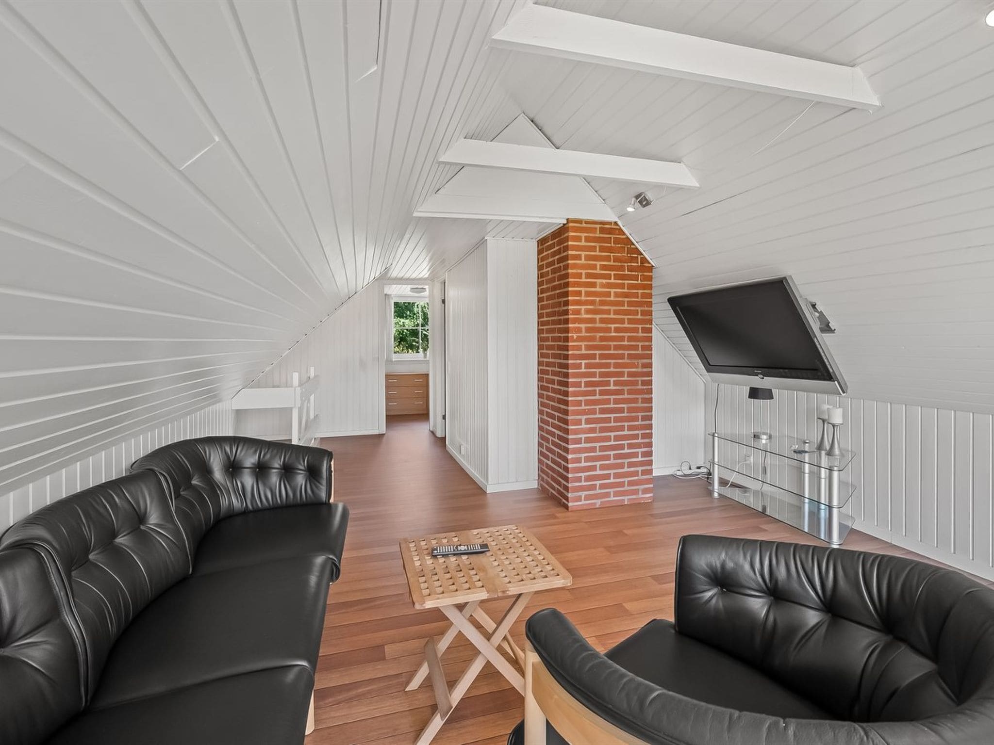 Un intérieur moderne avec un plafond en pente, une cheminée en briques, un téléviseur à écran plat fixé au mur et des canapés en cuir.