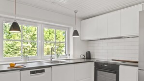 Uma cozinha moderna com armários brancos, máquina de lavar louça, forno e iluminação pendente.