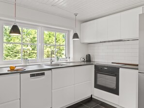 Eine moderne Küche mit weißen Schränken, einem Geschirrspüler, einem Backofen und Pendelleuchten.