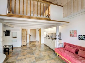 Ein geräumiger Loft mit hoher Decke, freiliegenden Holzbalken, einer Küchenzeile und einem roten Sofa.