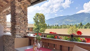 Ein Balkon mit steinernen Säulen, Korbmöbeln und einem Tisch, gedeckt mit einer Flasche und Gläsern.