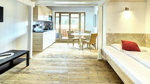 A room with a bed, a dining table with chairs, a kitchen area, and a view through a glass door. - Edelweiss 2 by Interhome (Kaprun)