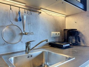 A modern kitchen with a stainless steel sink, a coffee maker, and hanging utensils. - Edelweiss 4 by Interhome (Kaprun)