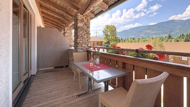 Ein Holzbalkon mit Tisch und Stühlen, der einen Blick auf eine gebirgige Landschaft bietet.