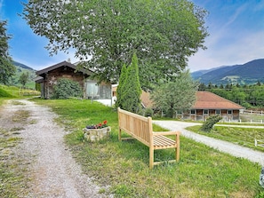 A rustic wooden cabin with a gravel path leading to a bench, surrounded by lush greenery and mountains in the background. - Edelweiss Suite 6 by Interhome (Kaprun)
