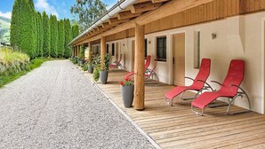 A wooden deck with red lounge chairs, a gravel path, and a row of potted plants. - Edelweiss Suite 6 by Interhome (Kaprun)