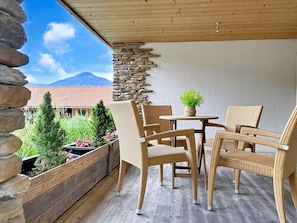 Eine Holzterrasse mit Korbmöbeln, einer Steinmauer und Blick auf einen Berg.