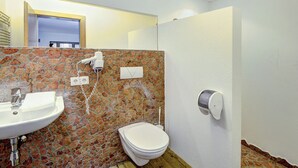 A bathroom with a stone wall, a sink, a toilet, and a shower. - Edelweiss Suite 6 by Interhome (Kaprun)