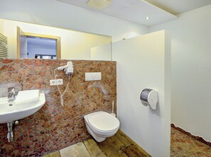 A bathroom with a stone wall, a sink, a toilet, and a shower. - Edelweiss Suite 6 by Interhome (Kaprun)