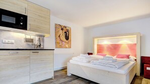 A modern bedroom with a white bed, a kitchen area with a microwave, and a painting on the wall. - Edelweiss Suite 6 by Interhome (Kaprun)