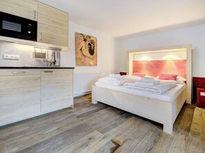 A modern bedroom with a white bed, a kitchen area with a microwave, and a painting on the wall. - Edelweiss Suite 6 by Interhome (Kaprun)