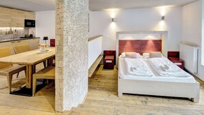 Un dormitorio con cabecera de madera, dos mesitas de noche, una cama con ropa blanca impecable, una mesa de comedor con sillas y una pared de piedra.