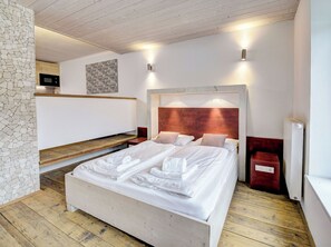 Ein Schlafzimmer mit einem hölzernen Bett, weißen Leinen, einer Steinwand und einem Holzboden.