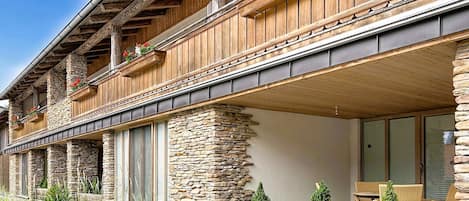 A two-story building with stone and wooden exterior, balconies with flower boxes, and a covered outdoor seating area.