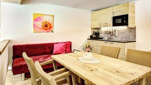 Uma área de jantar acolhedora com mesa de madeira, cadeiras de vime, um sofá vermelho e uma cozinha com armários de madeira e micro-ondas.