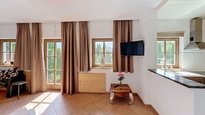 A modern kitchen with a flat-screen TV, a wooden dining table, and a view of the outdoors through large windows. - Edelweiss Suite 9 by Interhome (Kaprun)