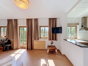 A modern kitchen with a flat-screen TV, a wooden dining table, and a view of the outdoors through large windows. - Edelweiss Suite 9 by Interhome (Kaprun)
