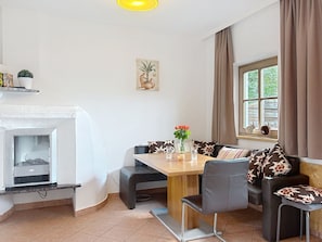 A living room with a fireplace, a dining table with chairs, a sofa with patterned cushions, and a window with curtains. - Edelweiss Suite 9 by Interhome (Kaprun)