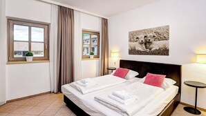 A hotel room with a large bed, two bedside lamps, a window with curtains, a wall-mounted picture, and a small table. - Edelweiss Suite 9 by Interhome (Kaprun)
