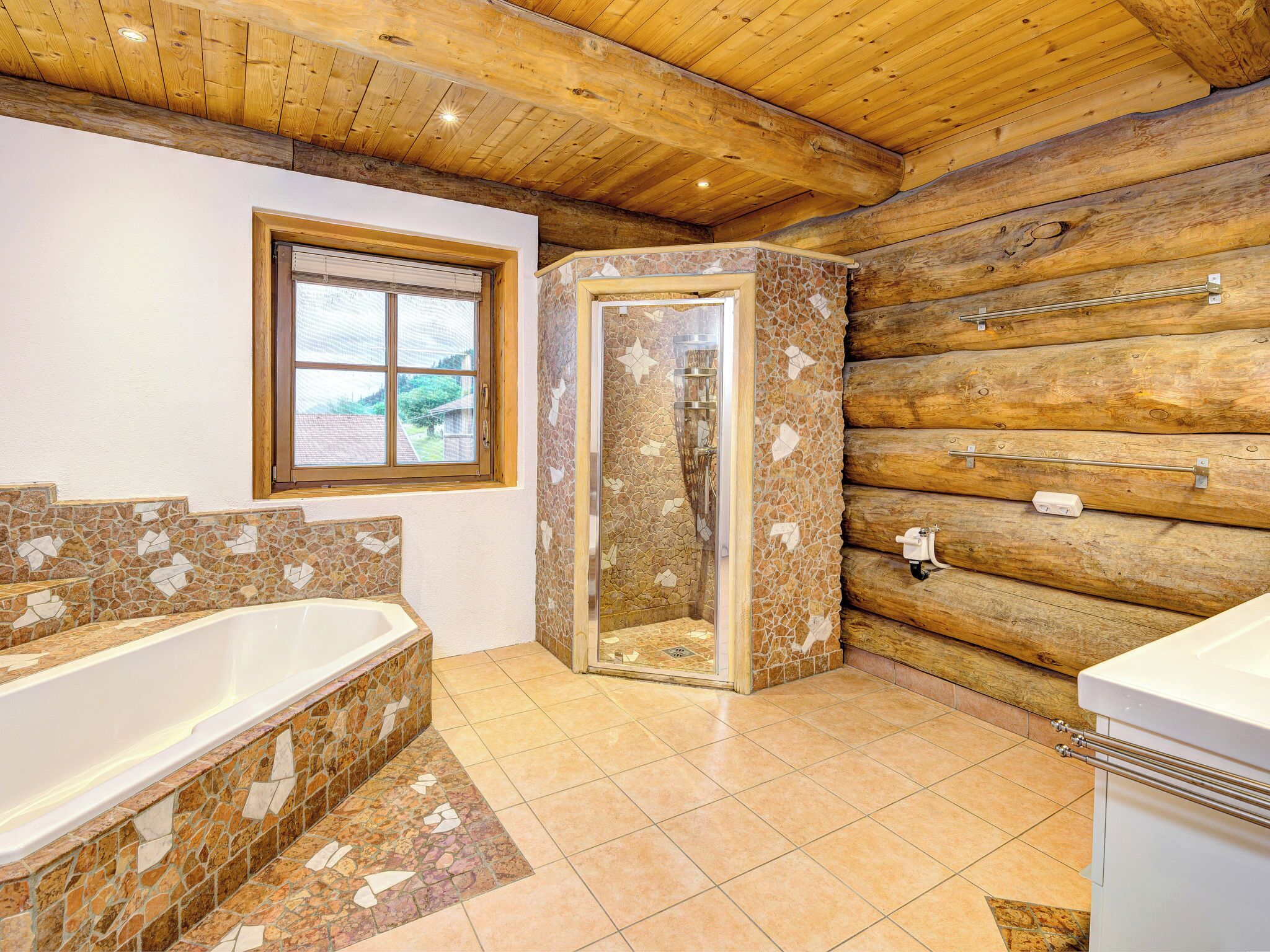 Ein Badezimmer mit Dusche aus Steinplatten, einer Badewanne und einem Fenster.