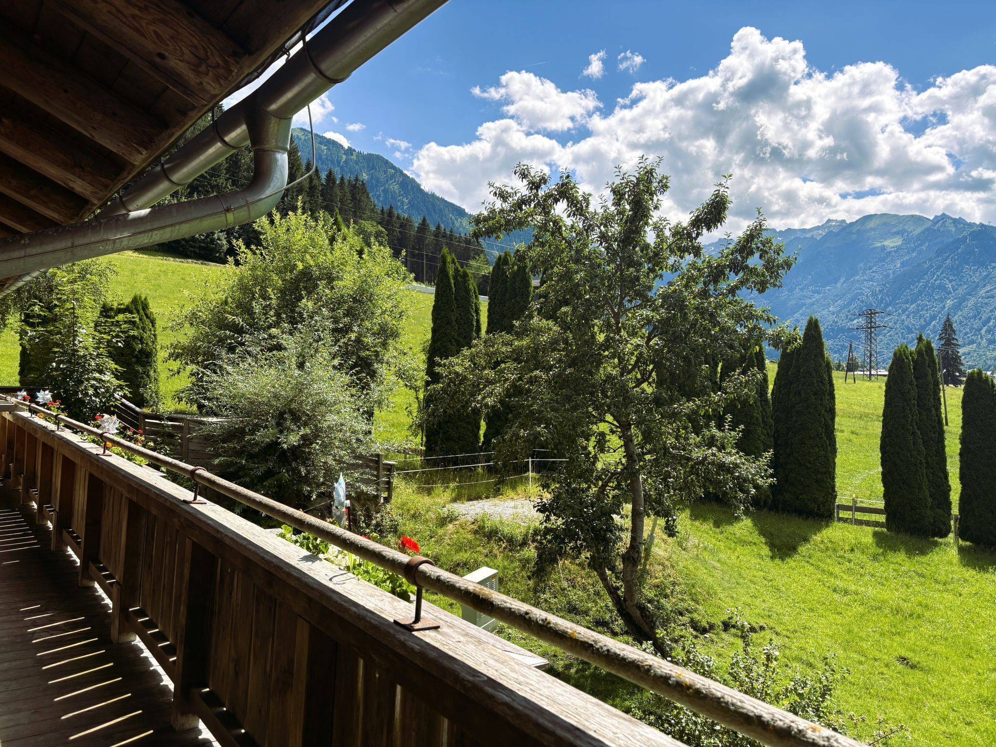 Ein hölzerner Balkon mit Blick auf ein grünes Feld, Bäume und Berge.