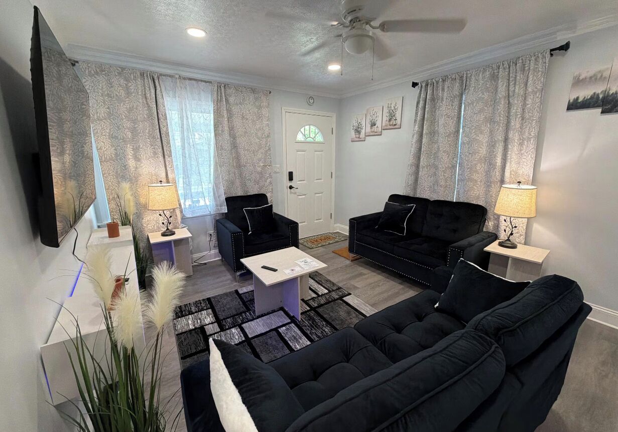 A modern living room with a black sofa, two armchairs, a coffee table, and a TV.