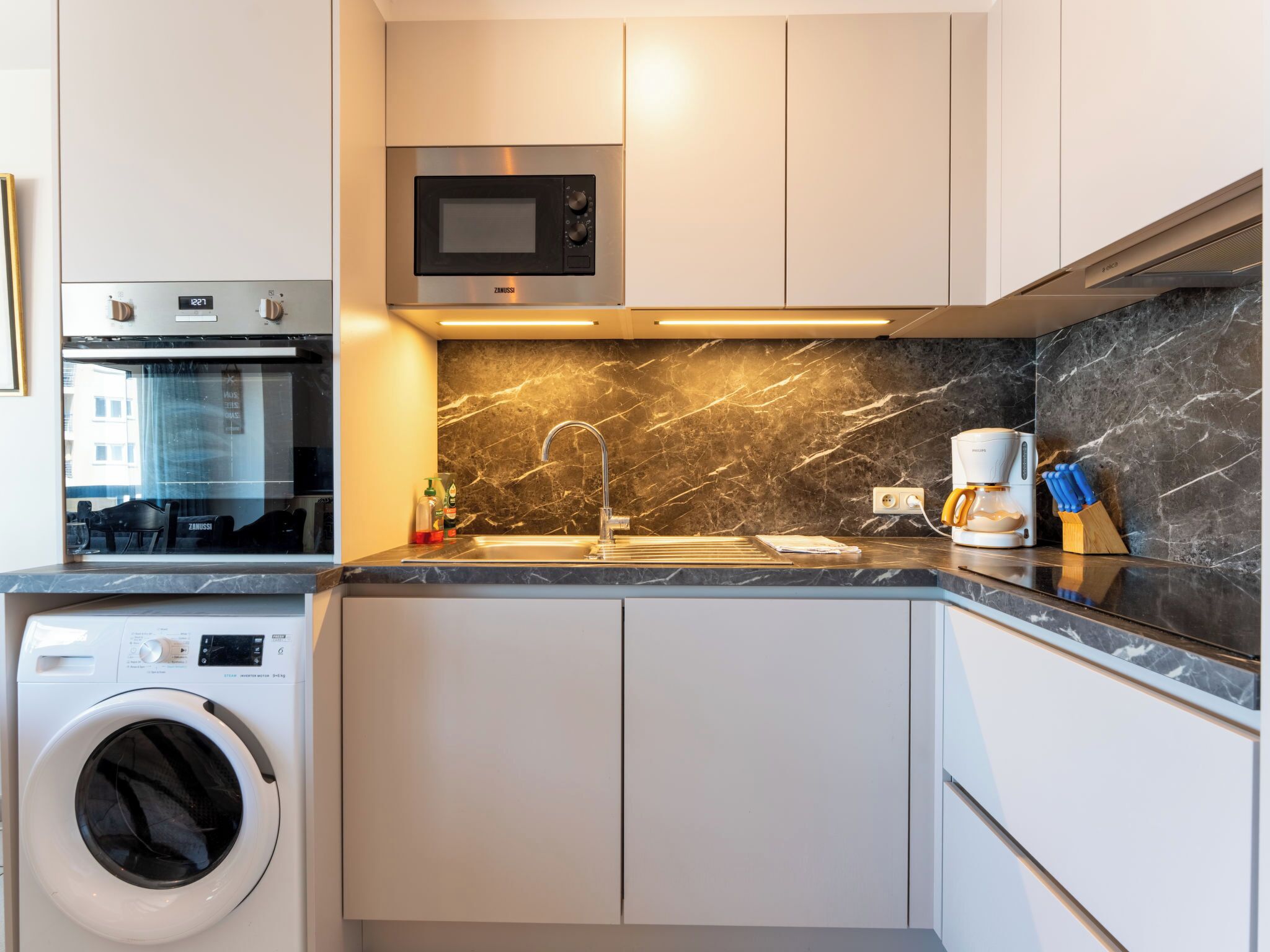 A compact kitchen with a built-in microwave, a coffee maker, and a washing machine.