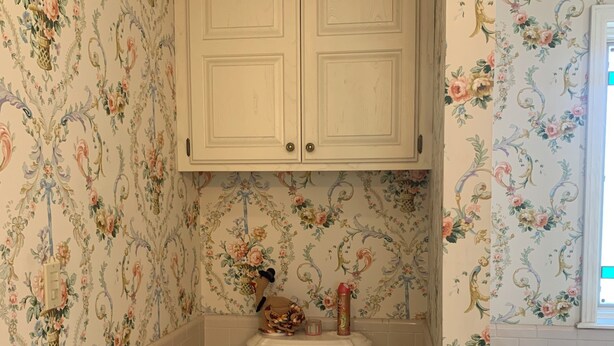A bathroom with a toilet, a trash bin, a cabinet, and a towel rack.