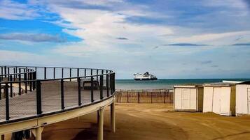 A beach with a pier, a ship in the distance, and beach huts.