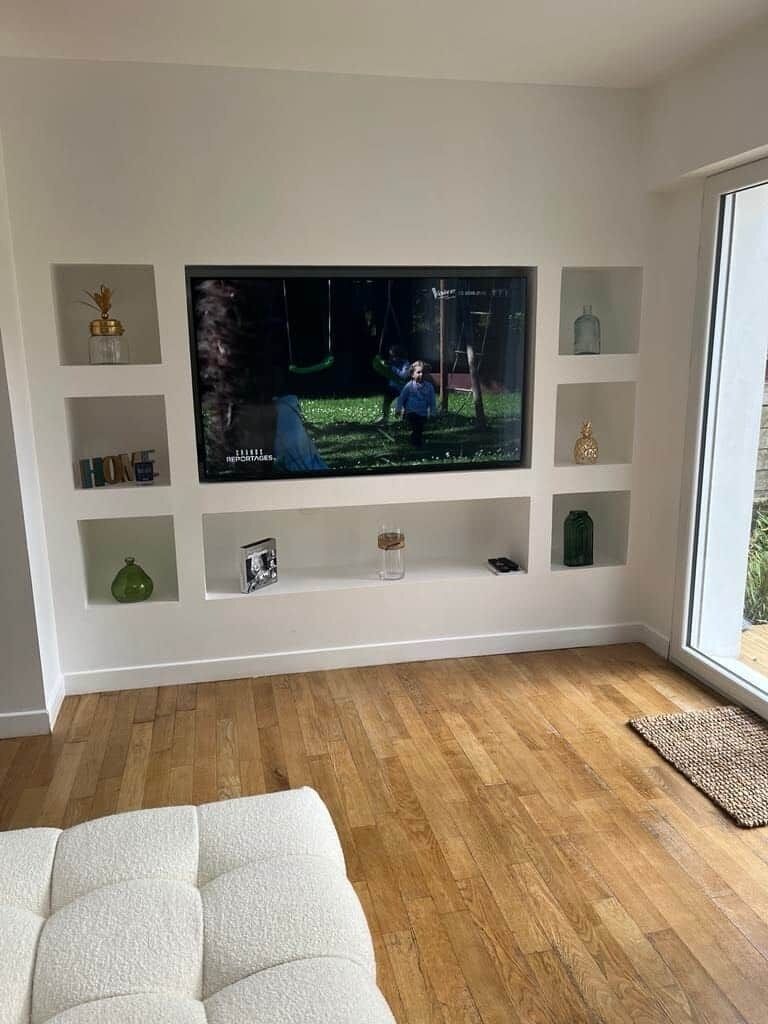 A modern living room with a flat-screen TV mounted on a white wall, wooden flooring, and a white sofa.