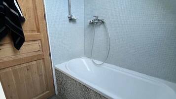 A bathroom with a bathtub, a shower, and a wooden door.