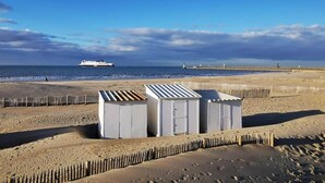 En strand med en række hvide, flytbare konstruktioner, et skib i horisonten og et træhegn.