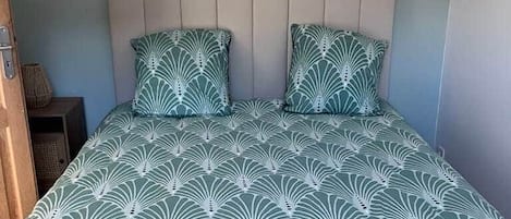 Uma cama com colcha estampada, cabeceira com vários painéis e decoração na parede com espelhos redondos.