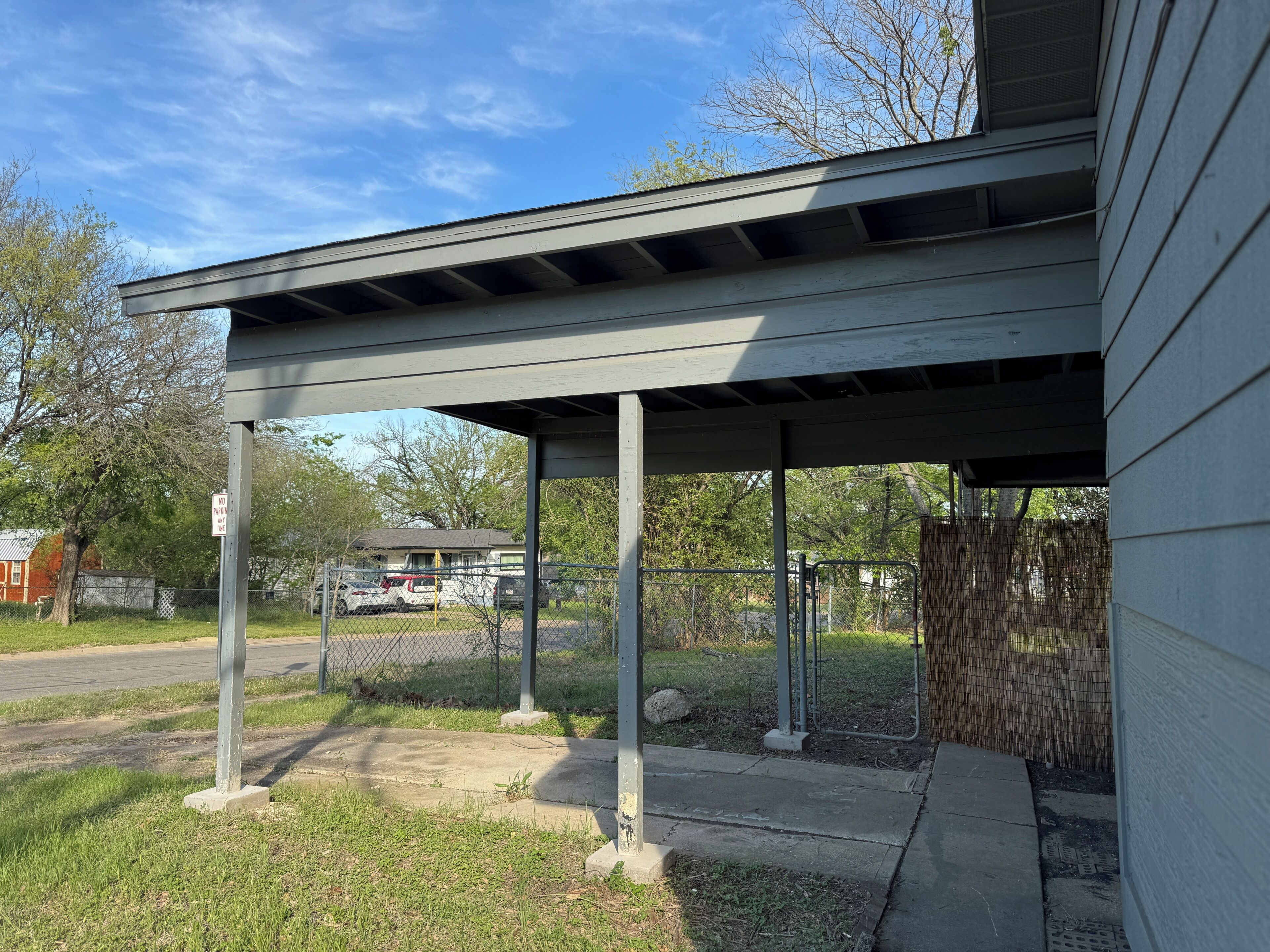 A covered outdoor area with a metal fence, a concrete pathway, and a 'NO PARKING ANY TIME' sign.