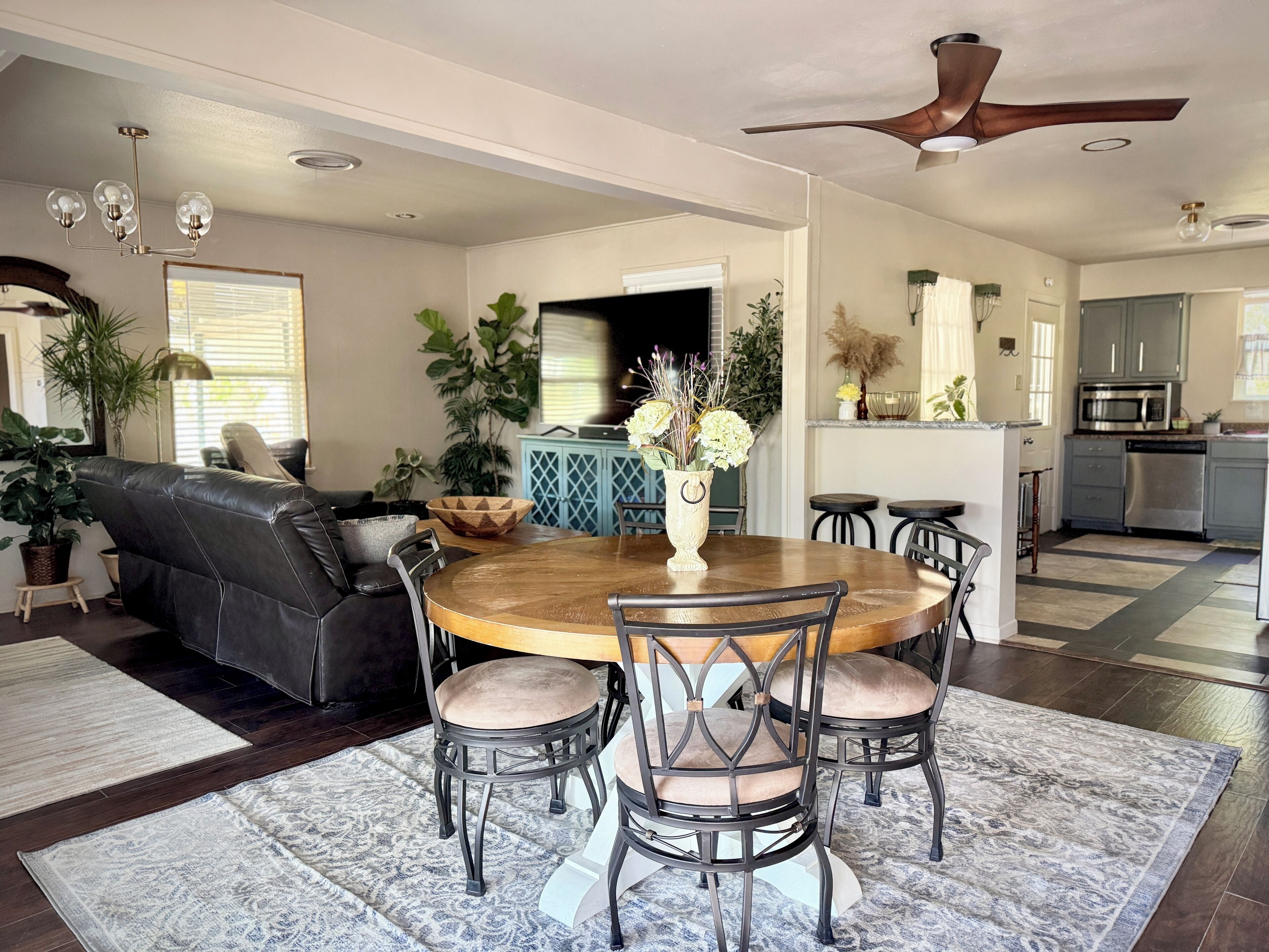 A modern living room with a dining area, a kitchen, and a ceiling fan.