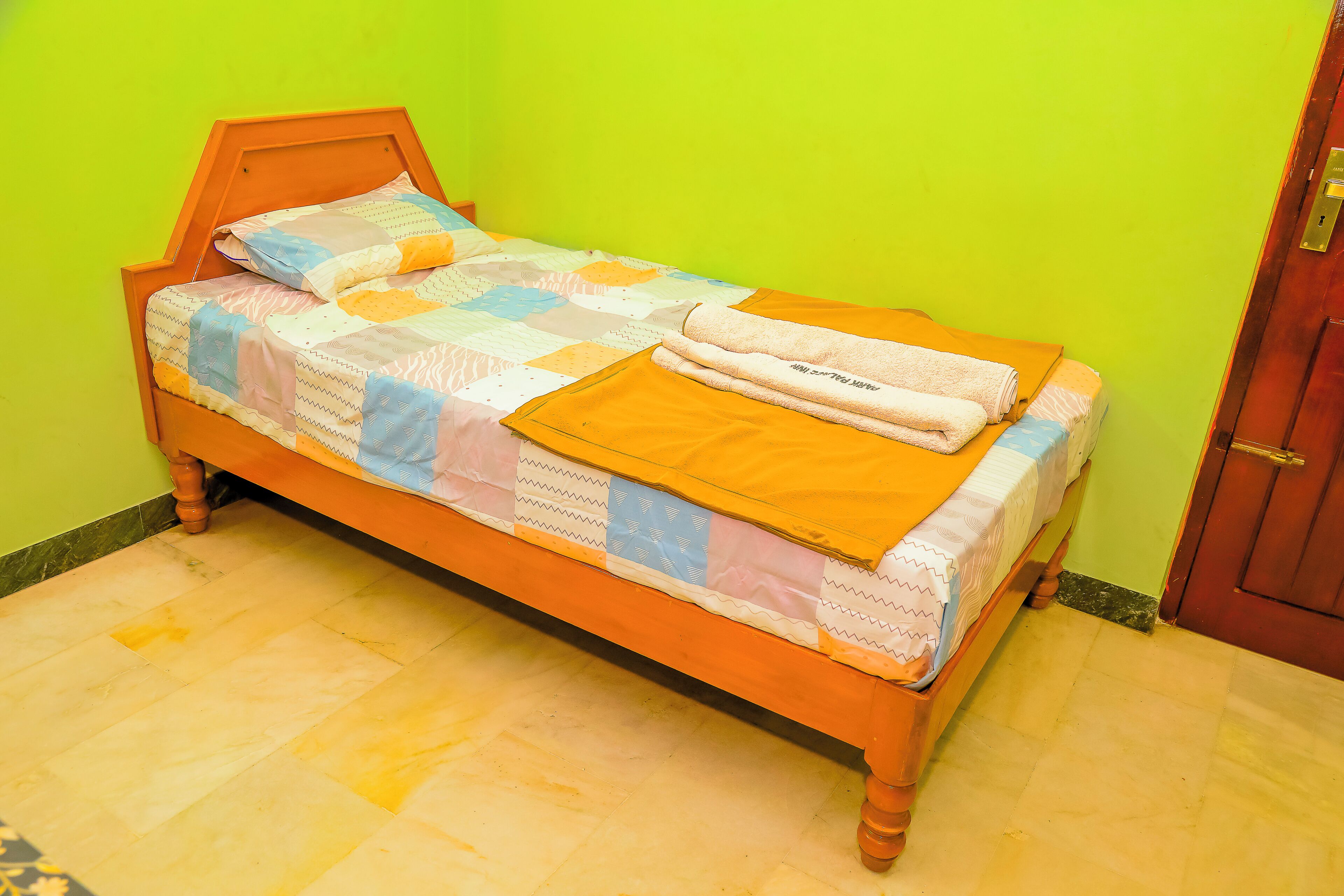 A single bed with a quilt, a folded towel, and a wooden headboard in a room with green walls and a wooden floor.
