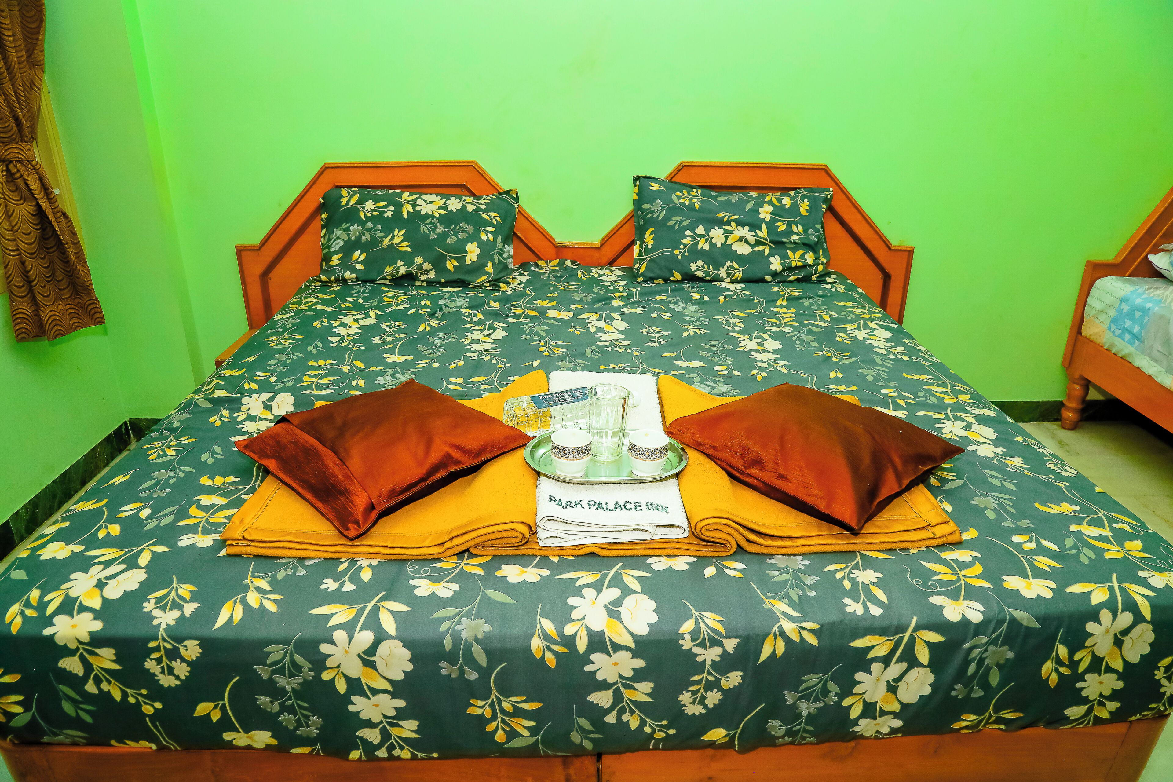 Un lit avec une literie à motifs floraux, deux oreillers, un plateau avec des verres et une pancarte indiquant « Park Palace Inn ».