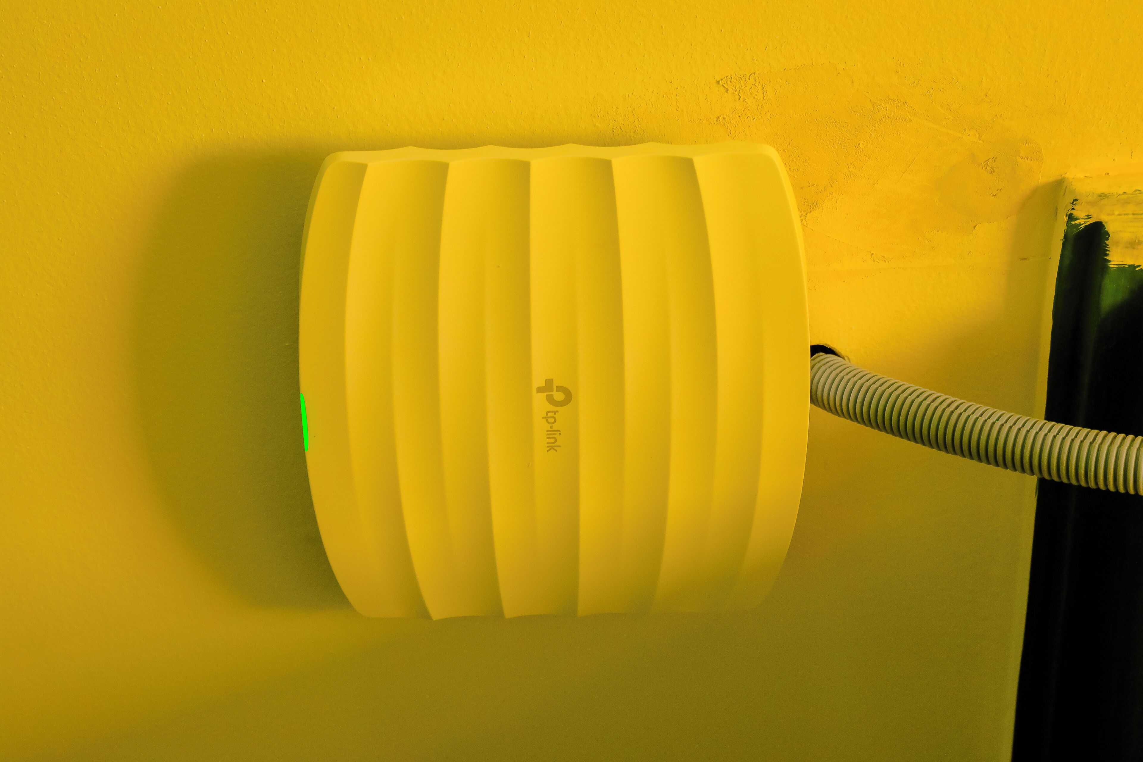 Un dispositivo amarillo fijado a la pared con un tubo flexible.